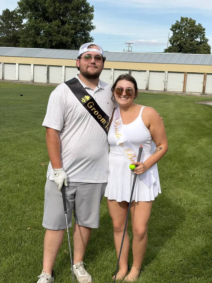 A bride-to-be and groom-to-be in sashes on the course